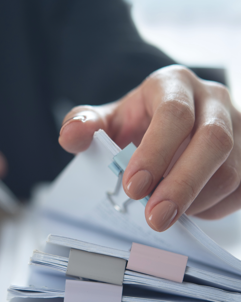 woman in black suit with beige nail varnish flicking through paperwork, image of hand an arm only. Fertility investigations