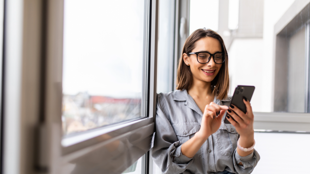 Side view portrait of a woman using a smartphone standing by a window at home
